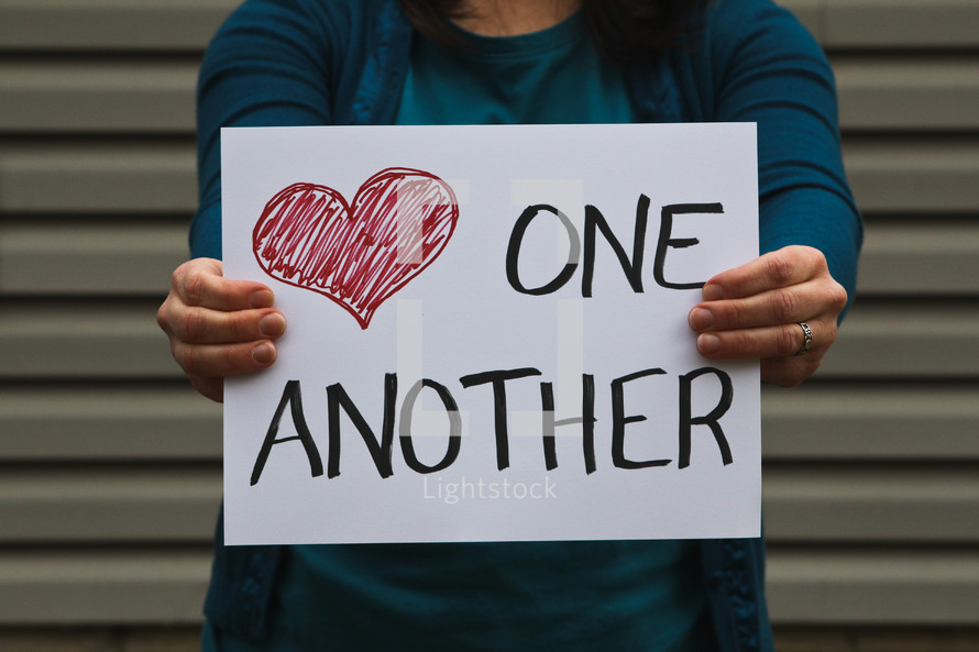 A woman holding a sign that says love one another.