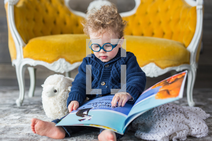 a child in glasses reading a book on the floor 