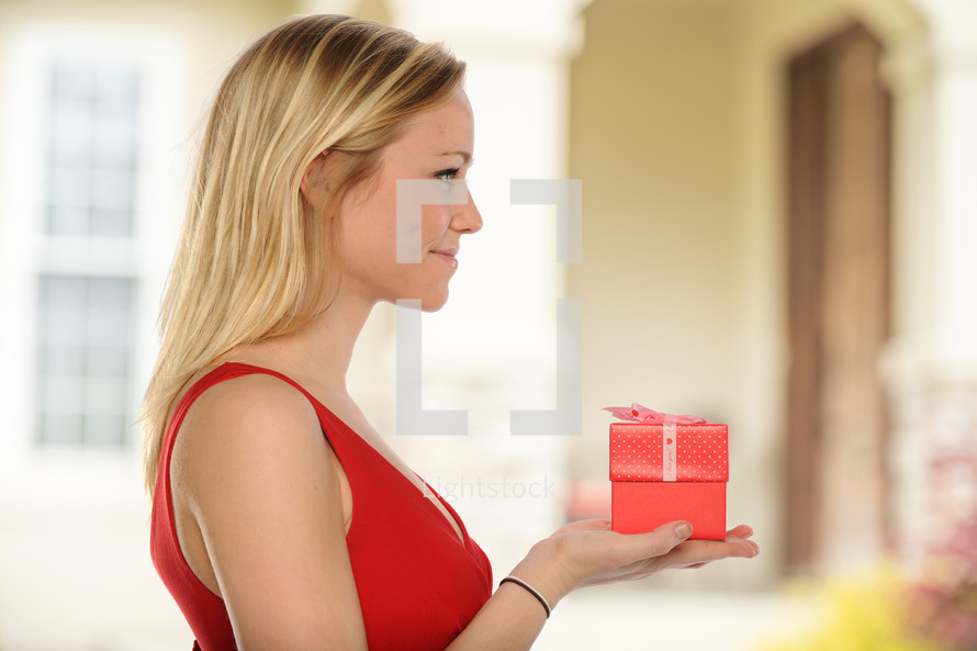 Young beautiful woman holding a gift with house out of focus as background