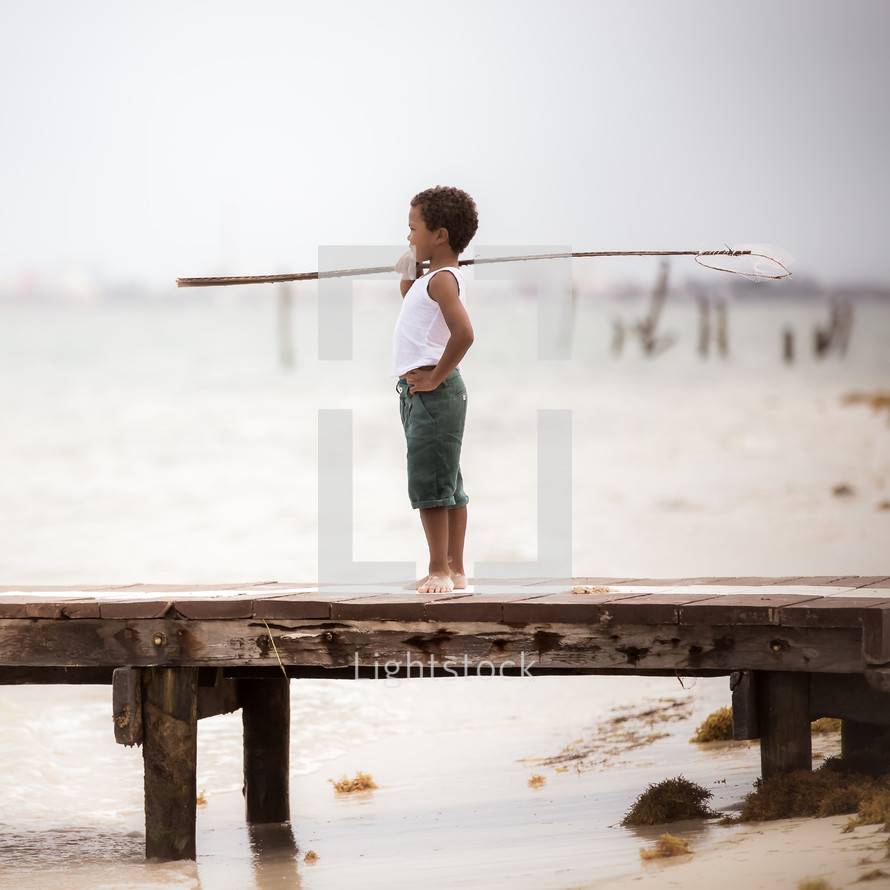a boy holding a fishing net standing on a dock 