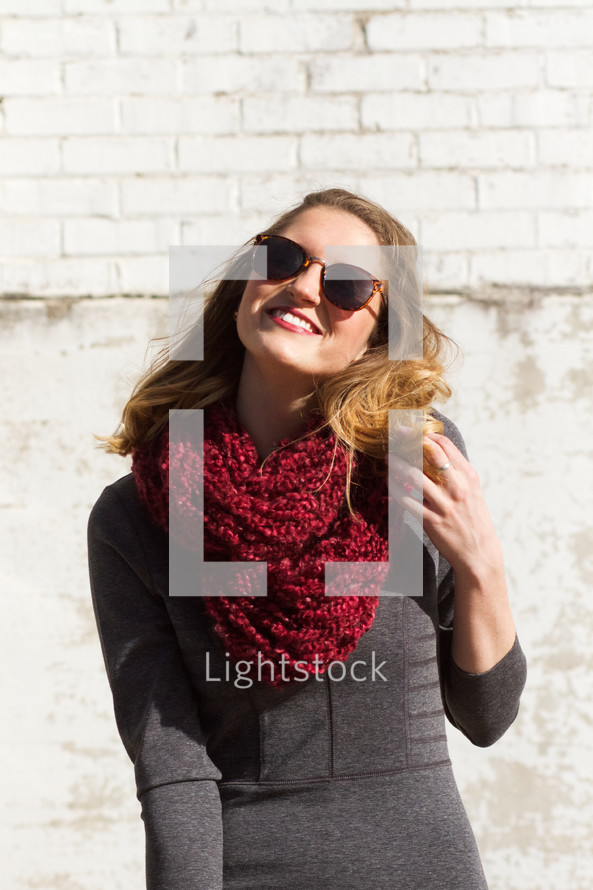 woman smiling outdoors in a scarf and sunglasses 
