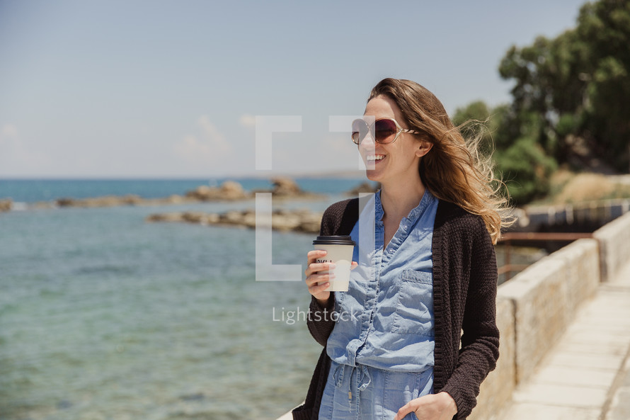 woman walking holding a coffee cup outdoors along the coast in Greece 