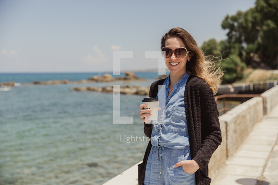 woman walking with a coffee cup along the coast in Greece 