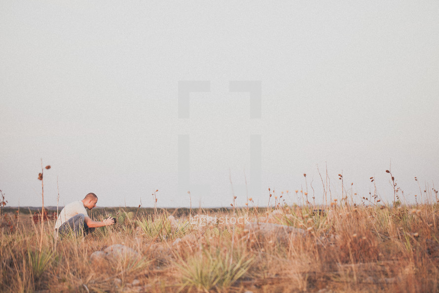Man with camera crouching in a field of tall grass.