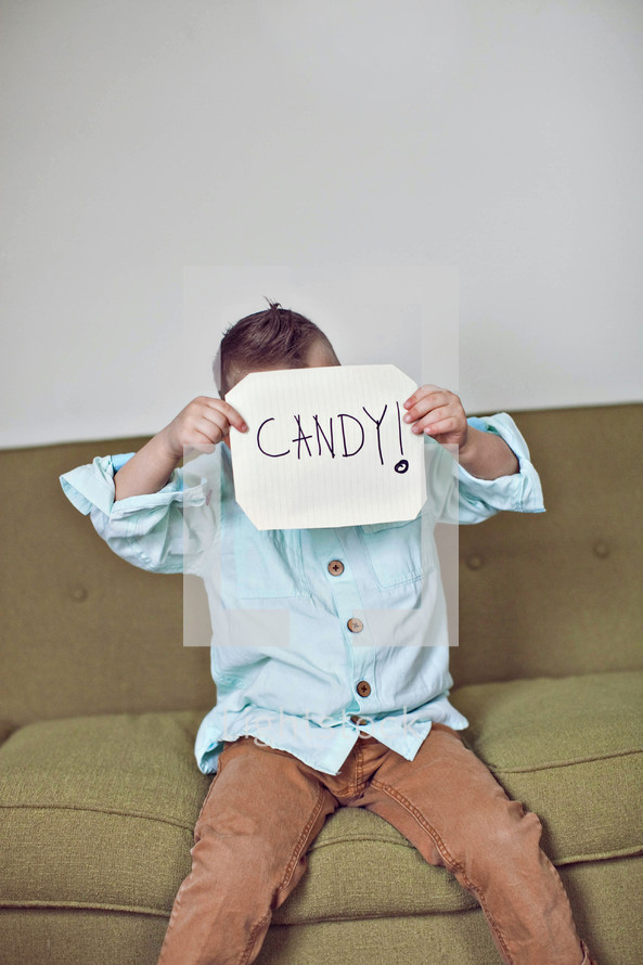 a boy child holding up a sign that reads Candy 