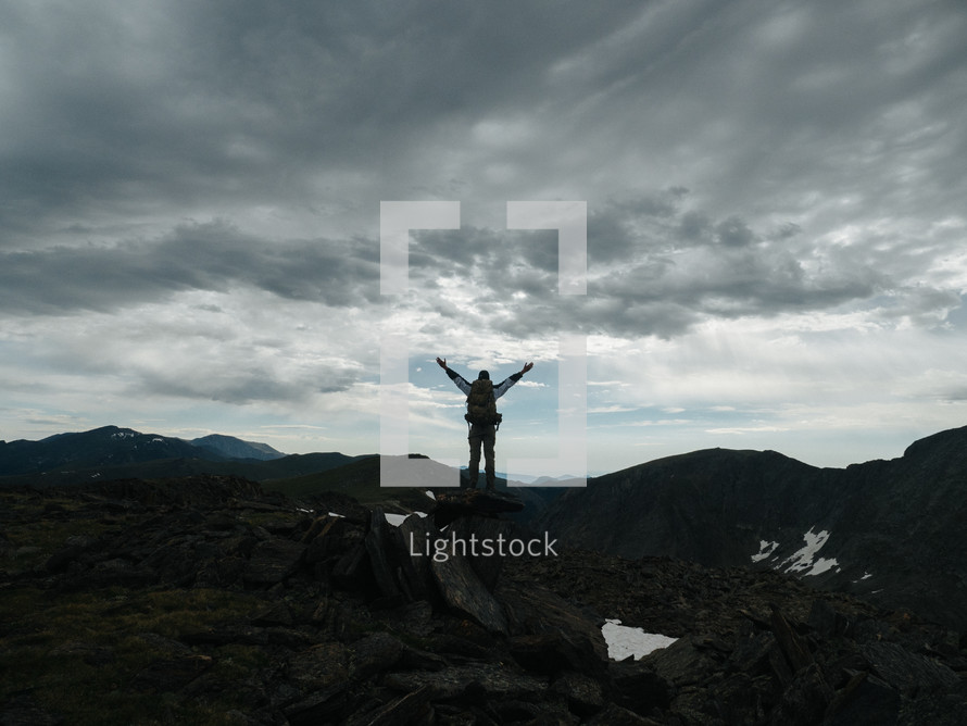 man standing on a mountaintop with raised arms 