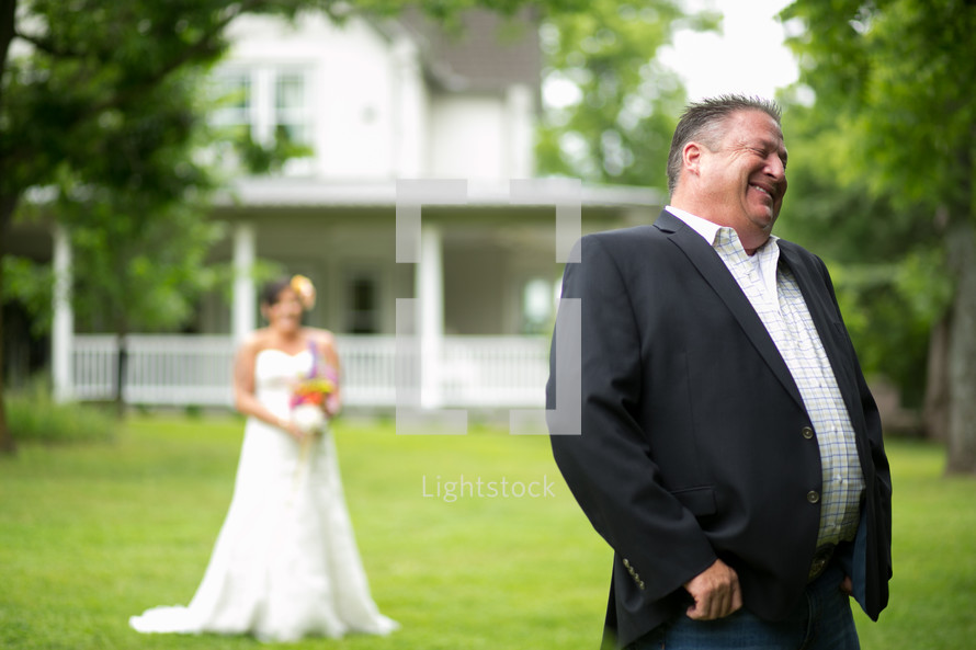 A smiling groom with his eyes closed and back to his bride.