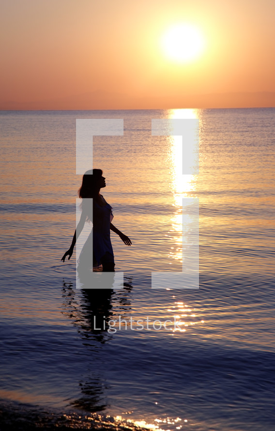 a woman standing in the ocean at sunset 