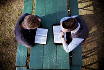 two men reading the Bible sitting at a picnic table 