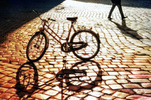 Shadow of a bike on cobblestone pavement at morning.
