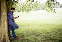 a man reading a Bible standing under a tree 