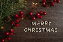 red berries and fairy lights on a wood background and words Merry Christmas 