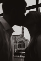 Couple kissing in front of large window