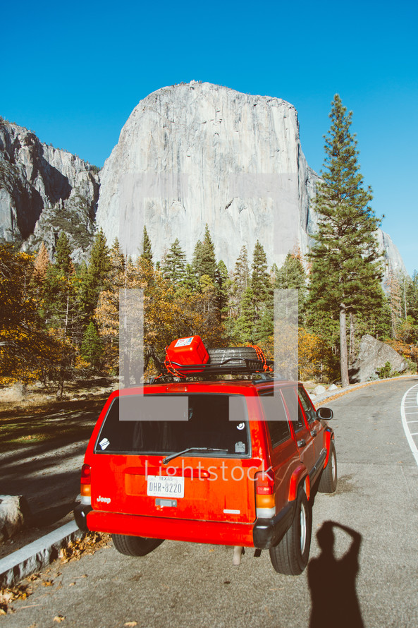 red SUV parked on the side of a road and view of a steep rock formation 