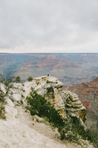 people sitting at the edge of a cliff looking out over a canyon 
