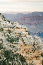 people standing on the edge of a cliff looking out over a canyon 