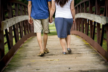 couple walking holding hands across a bridge 