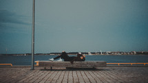 a man sleeping on a bench in a harbor 