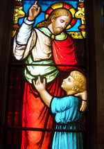 A stained glass window of Jesus and child  together as Jesus points to Heaven. Beautiful stained glass window with red, blue, gold, yellow colors. Jesus said 'Suffer the little children to come unto me' as it takes the faith of a child to believe and trust in Christ for eternal salvation. 