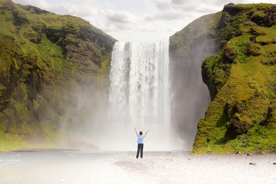 a person  standing in front of a waterfall with arms raised 