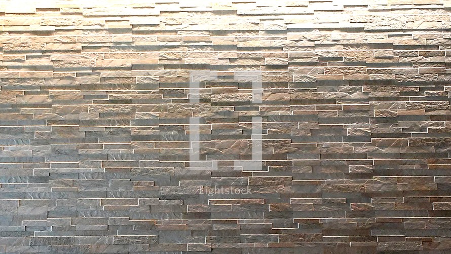 A stone brick wall background from an office building that is back lit with light and has a consistent brick stone face pattern.