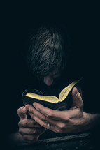 Man praying with head bowed before an open Bible held in both hands.