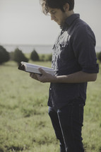 a man standing outdoors in a field reading a Bible 