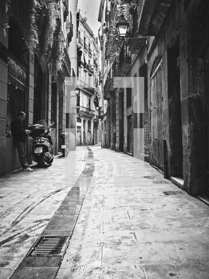A man texting next to a scooter in a narrow alley in Barcelona 