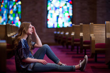 Young woman or teen sitting in aisle of a church meditating with pleasant expression.
