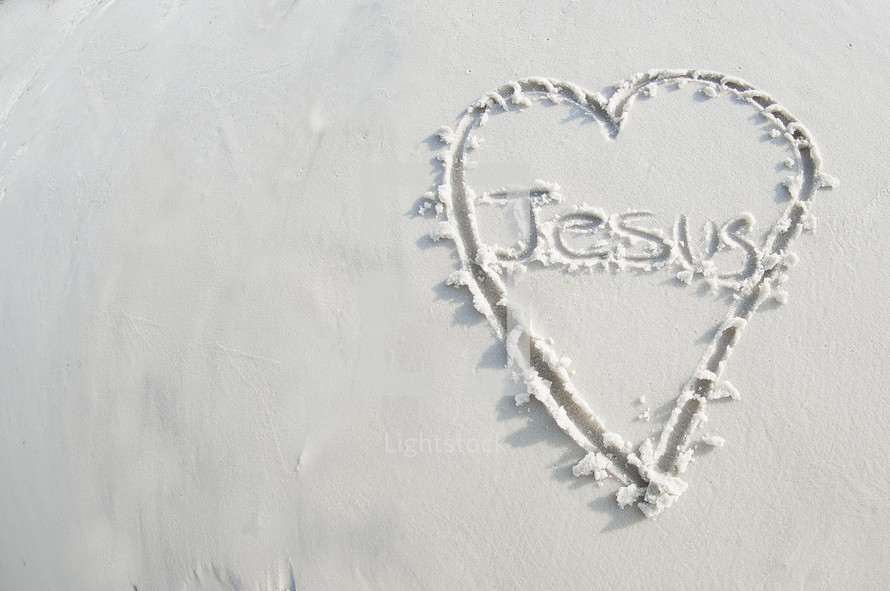 The word "Jesus" inside a heart drawn in the sand.