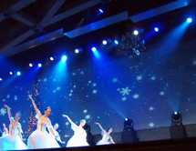 A group of four ballet dancers performing the nutcracker ballet against a blue background with snow flakes and white snow on a stage at a local church during Christmas time.  