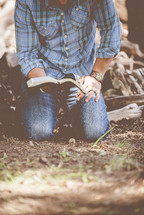 man kneeling and reading a Bible 