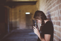 a man leaning against a brick wall reading a Bible and praying 