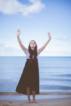 a woman with hands raised standing on a beach 