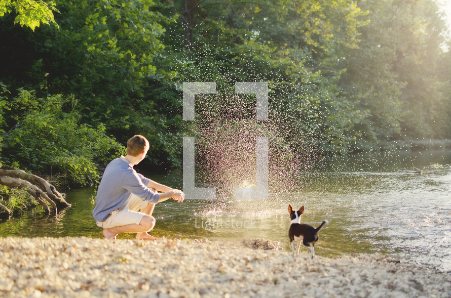Boy with dog skipping rocks on river