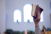 a hand holding up a Bible during a worship service 