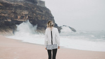 woman standing on a beach and waves crashing into rocks 