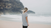 a woman in a striped shirt standing on a beach 