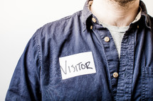 Man in a denim shirt with a visitor's tag.
