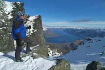 man standing on top of snow capped mountain ridge overlooking river