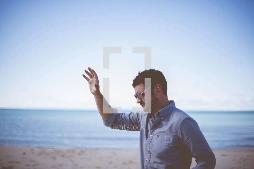 man with hand raised standing on a beach 