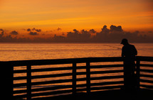 silhouette of a man fishing on a pier