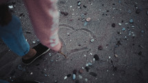 a woman drawing a heart in the sand 