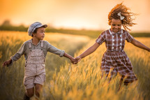 siblings running through a field holding hands 
