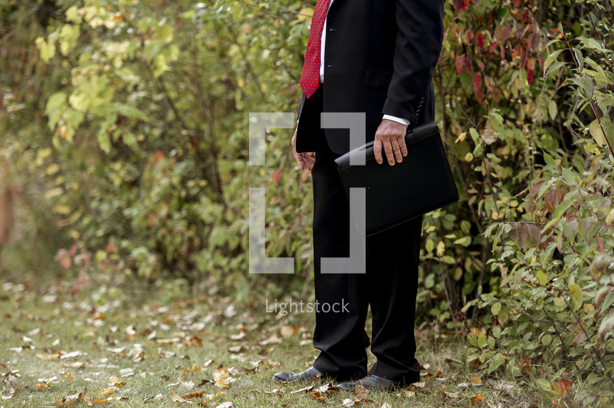 businessman holding a binder standing outdoors 