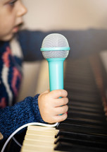 child holding a microphone over a piano 