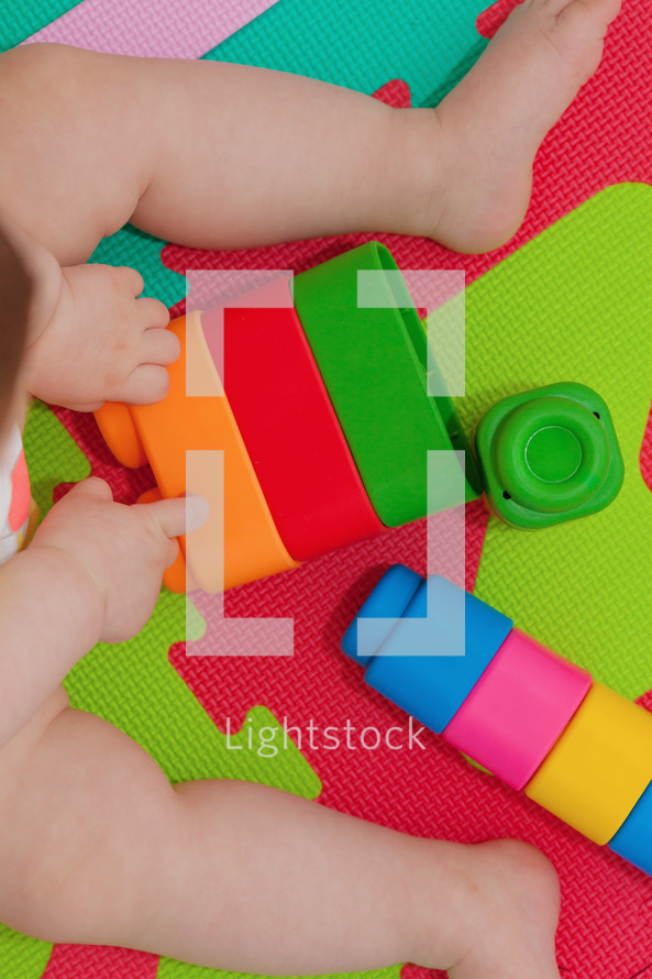 toddler plays with building block on the colored rubber mat
