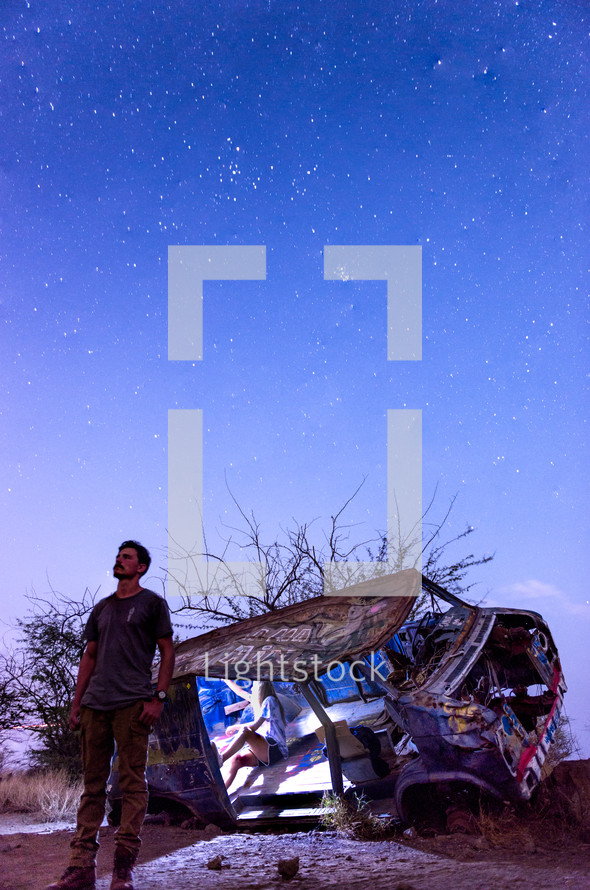 a man standing in front of an abandoned van under the stars at night 