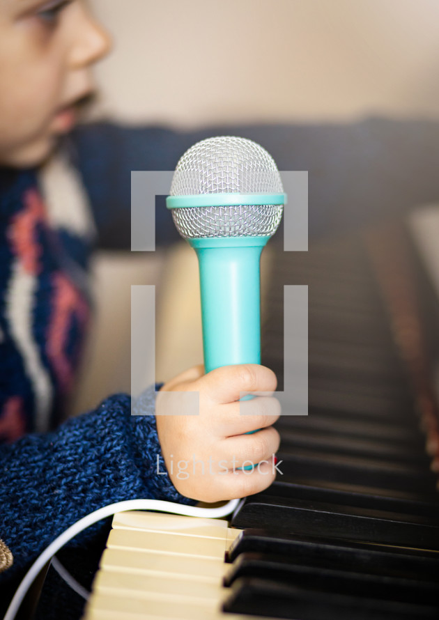 child holding a microphone over a piano 
