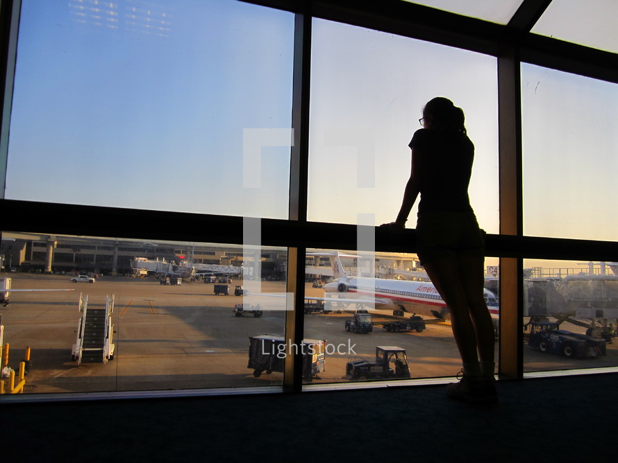 woman looking out airport windows at the terminal and runway 